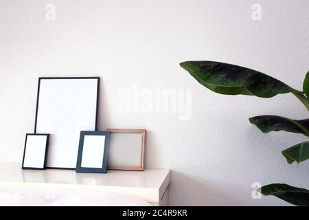 Empty wooden frames on white shelf near white wall and green house plant modern interior, scandinavian style room Stock Photo