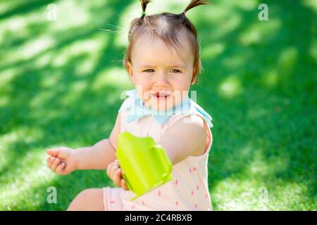 Toddler girl drinks water from plastic bottle sitting in summer on grass Stock Photo