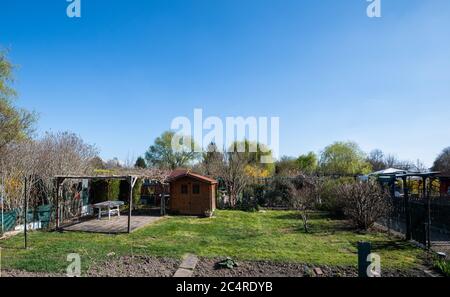 Empty garden allotment with large grass lawn and small wooden house in background - hobby agriculture Stock Photo