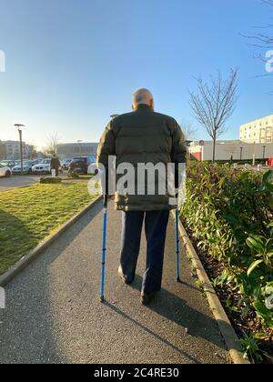 Strasbourg, France - Jan 20, 2020: Rear view of senior man walking with canes in large French hospital parking Stock Photo