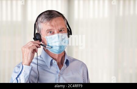 Senior caucasian man wearing facemask using headset to talk to customers or team during coronavirus epidemic Stock Photo