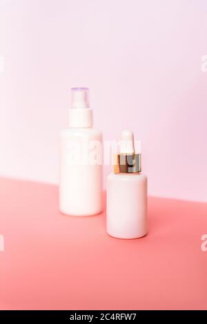Two bottles with serum and cosmetic lotion on pink table against white wall. Unbranded blank packages. Natural skincare products concept. Selective fo Stock Photo