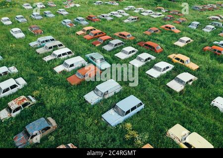 Old rusty abandoned retro cars in green meadow, aerial view from drone. Stock Photo