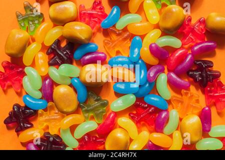 Multi-colored glazed jelly beans sweets on orange paper background. Stock Photo