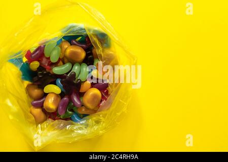 Multi-colored glazed jelly beans sweets in plastic package on yellow paper background. Stock Photo
