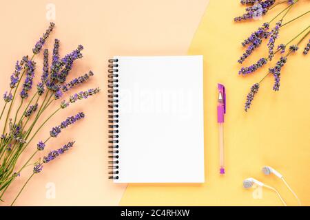 Mock up with blank notepad on yellow background with lavender flowers, pen and earphones. Top view, flat lay Stock Photo