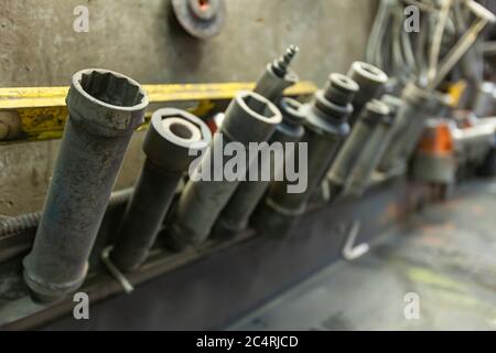 Industrial drill bits of various shapes and size in a concrete plant factory tools storage above the workbench. With some blurry tools in the background Stock Photo