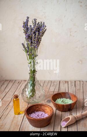 Bottle with essential oil and bowls with sea salt on wooden table. Lavender cosmetics, spa and aromatherapy concept Stock Photo