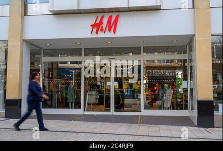Bromley (Greater London), Kent, UK. H&M store in Bromley High Street with a blurred pedestrian walking past. H&M shop with reflections in the windows. Stock Photo