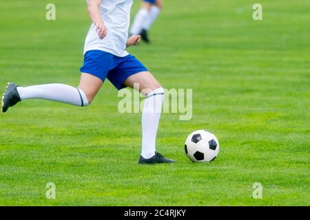 Young woman soccer player kicks ball on football field. Team sport concept. Stock Photo