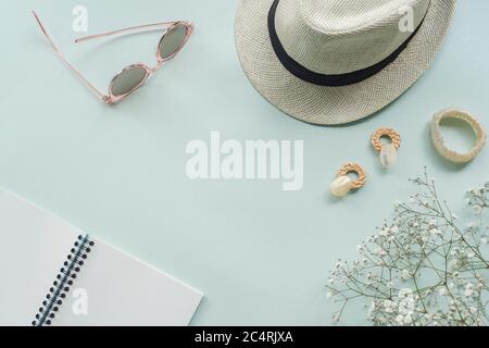 Flat lay with women's accessories on blue background. Sunglasses, straw hat, earrings, bracelet, notepad and gypsophila flowers. Top view, copy space. Stock Photo