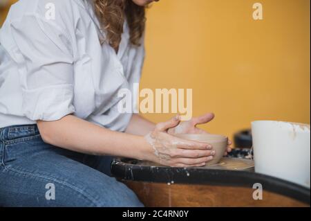 The female potter finished making a clay vase remove it from the potter's wheel. Creating vase of white clay. Making ceramic products from white clay Stock Photo
