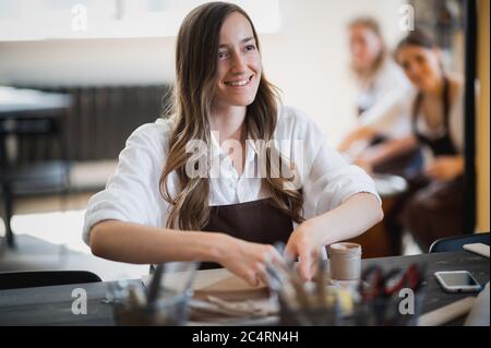 Young woman curving clay product edges Pottery workshop. Stock Photo