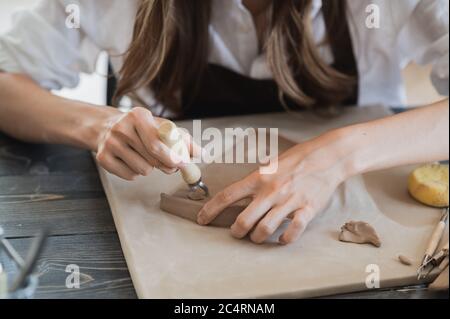 Close up of skilled craftswoman removing part of clay while making ceramic product in pottery workshop Stock Photo