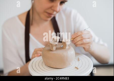 Female hands holding stick and making ornament on decorative product. Clay master moulding clay on a pottery and ceramics workshop. Stock Photo