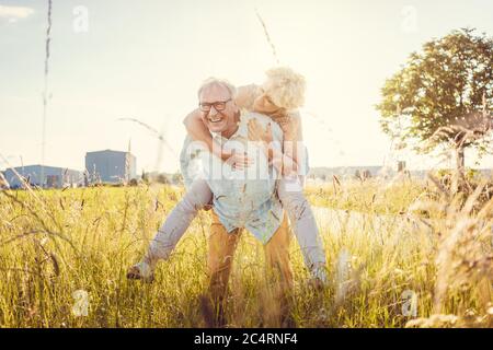 Strong senior man carrying his wife piggyback without back pain Stock Photo