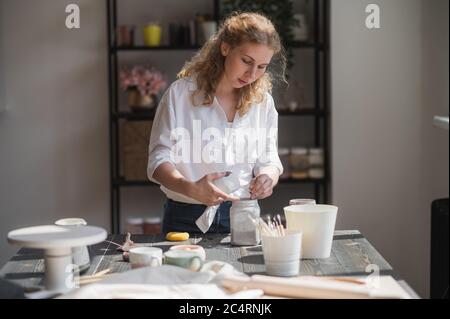 Close up of a woman making ceramic and pottery tableware at the workshop, working with clay and glaze. Stock Photo