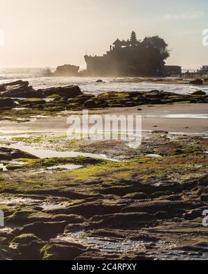 Backlit outline of Pura Tanah Lot Balinese sea temple with crashing waves on the pebble beach, Denpasar, Bali, Indonesia Stock Photo