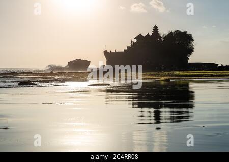 Backlit outline of Pura Tanah Lot Balinese sea temple with crashing waves on the pebble beach, Denpasar, Bali, Indonesia Stock Photo