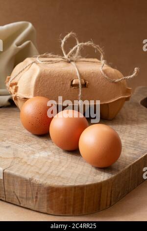 Three brown eggs on top of a kitchen table with an egg cup in the background. Beige tones. Symmetrical view Stock Photo