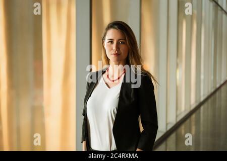 Young Business Woman Standing In Corporate Corridor Stock Photo