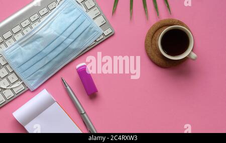 Top view of pink office desk with keyboard, medical face mask, coffee and stationery. Copy space. Stock Photo