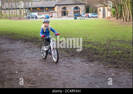 A young girl rides a bike along a country track. A car park in the background Stock Photo