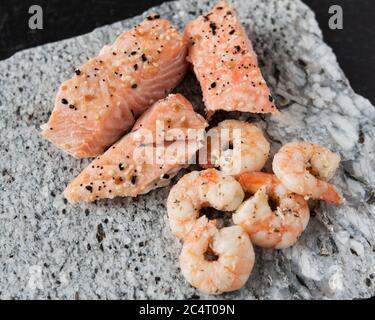 Broiled shrimp and salmon with everything bagel seasoning on a granite slab cutting board and a black slate background. Stock Photo