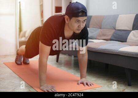 Asian male doing exercise at home to stay healthy on new normal lifestyle, indoor home workout concept, push ups plank position Stock Photo