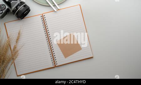 Top view of open blank notebook with sticky note on dinning table with camera, plate, silverware and copy space Stock Photo