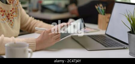 Side view of female designer using digital tablet while sitting at worktable with laptop and designer supplies Stock Photo