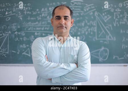 Portrait of serious male teacher standing against blackboard teaching mathematics in classroom, school and education concept. Stock Photo