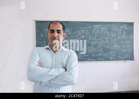 Male teacher standing against blackboard teaching mathematics in classroom, school and education concept. Stock Photo