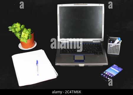Closeup shot of a laptop, phone, plant, notebook and pen box on black background Stock Photo