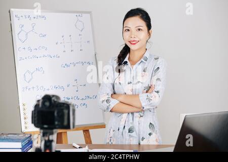 Portrait of smiling confident science teacher standing at whiteboard with chemical formulas and looking at camera after finishing online lesson Stock Photo