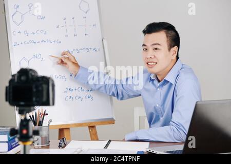 Science teacher drawing chemical formulas on whiteboard when hosting online lesson for college students Stock Photo