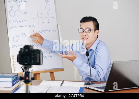 Young Asian chemistry teacher explaining formulas on whiteboard when hosting online class for school students Stock Photo