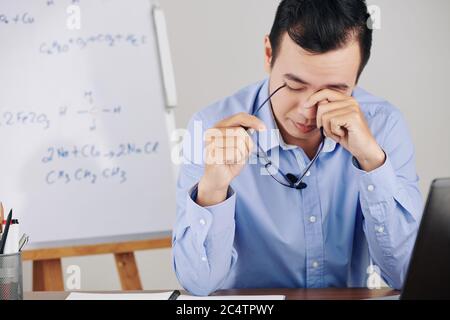 College teacher rubbing tired eyes after hosting remote class for his students Stock Photo