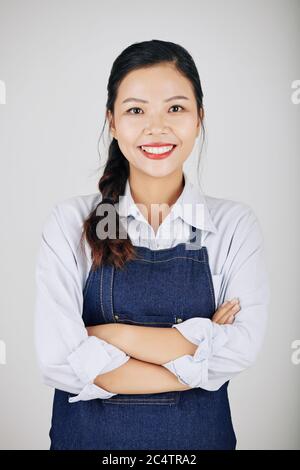 Portrait of young pretty Asian cafe waitress folding arms and smiling at camera Stock Photo