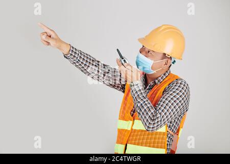 Contractor in medical mask using walkie-talkie when controlling work on construction site Stock Photo
