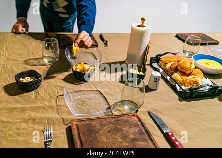 man holding french fries at a family home table prepared to celebrate the gathering of friends, with sauces, cheese, wine and dishes. Stock Photo