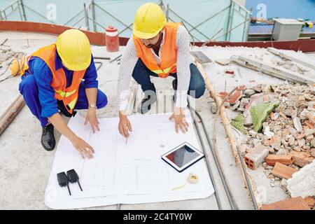 Engineers in hardhats discussing details of house blueprint when working at construction site Stock Photo