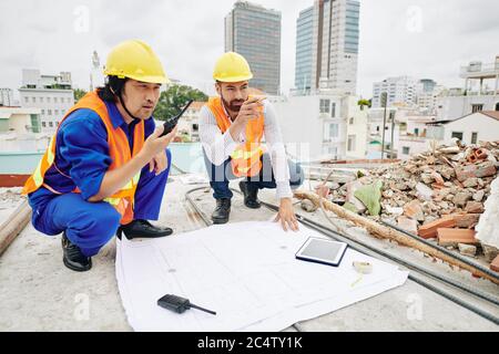Construction engineer pointing at building wall when contractor using walkie-talkie to explain employee what to do Stock Photo
