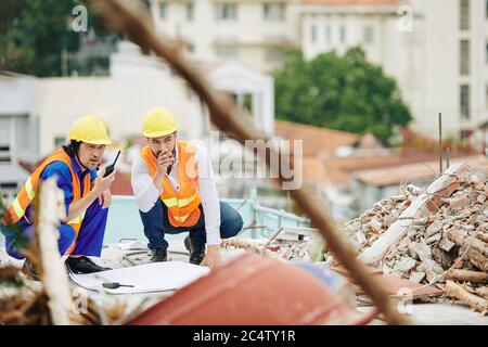 Engineers in bright orange vests and hardhats discussing work at construction site Stock Photo