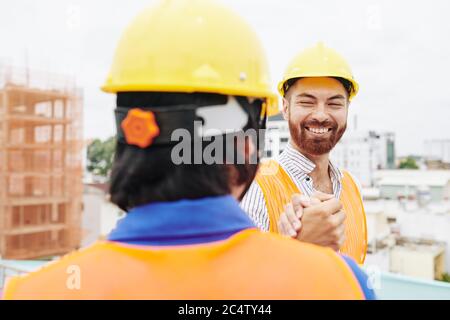 Happy smiling head engineer shaking hand of contractor when meeting at construction site in the morning Stock Photo
