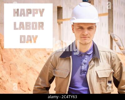 Happy Labor Day. Caucasian civil engineer or construction worker in white hardhat stands opposite construction site. Stock Photo