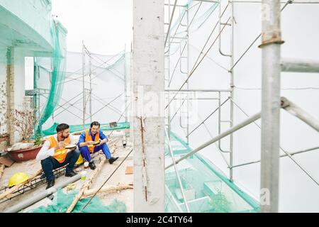 Construction workers eating lunch and joking around during break at site Stock Photo