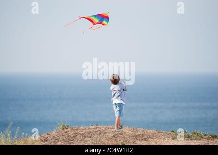 one little kid with flying color kite in air above blue ocean and sky in summer leisure games