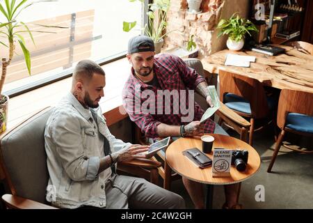 Pensive young man using digital tablet while planning trip with friend in coffee shop Stock Photo