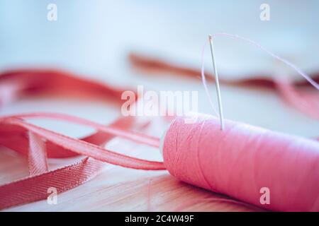 Pink spool of thread and a needle in it, side view on the table. Stock Photo